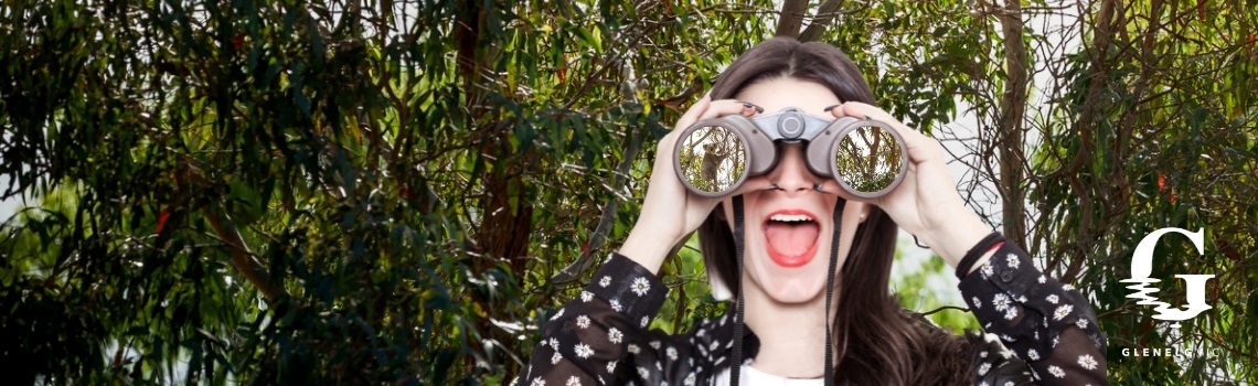 lady looking through binoculars in woods